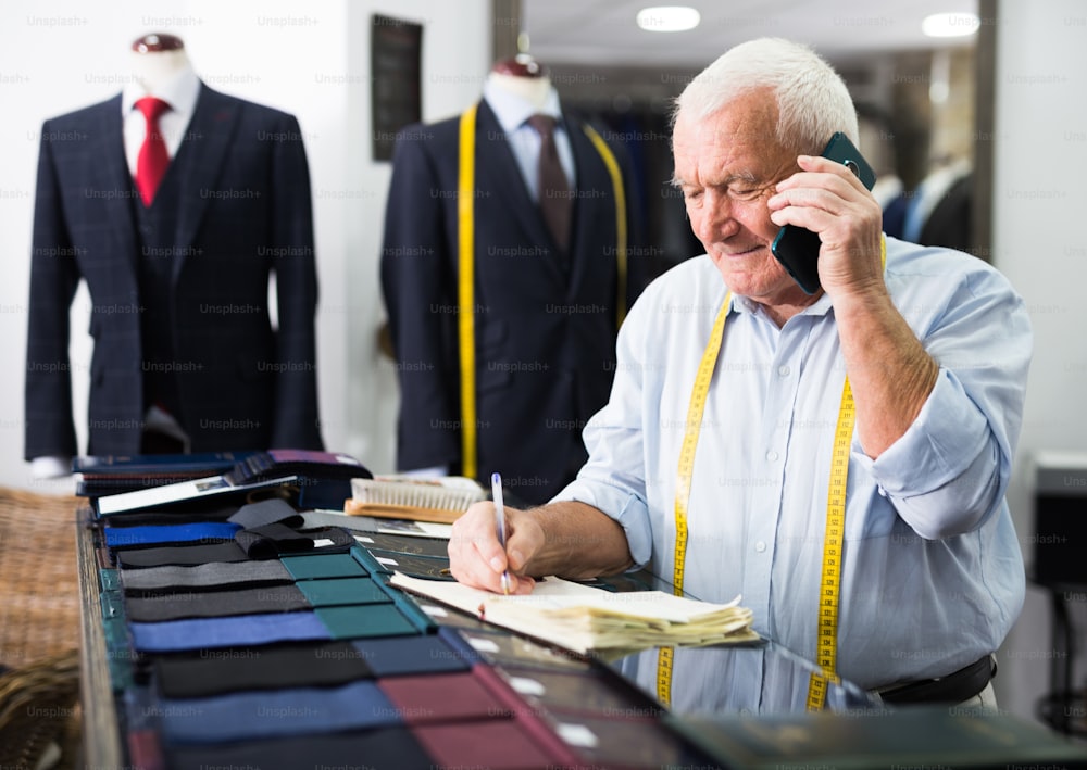 Professional tailor communicates with the client on mobile phone and takes notes in a notebook