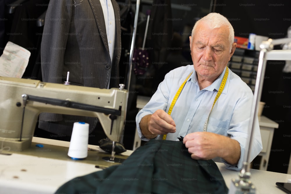 Elderly tailor sews lapel to a jacket in his workshop