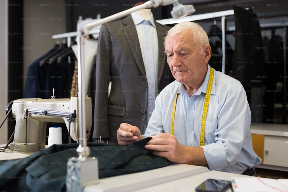 Elderly tailor sews lapel to a jacket in his workshop