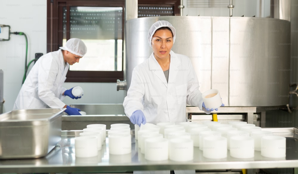 Woman wearing uniform showing cottage cheese production process on dairy factory