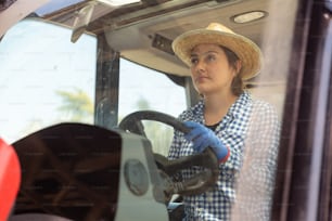 Portrait of skilled young hispanic female farmer working on farm on sunny summer day, driving small  tractor