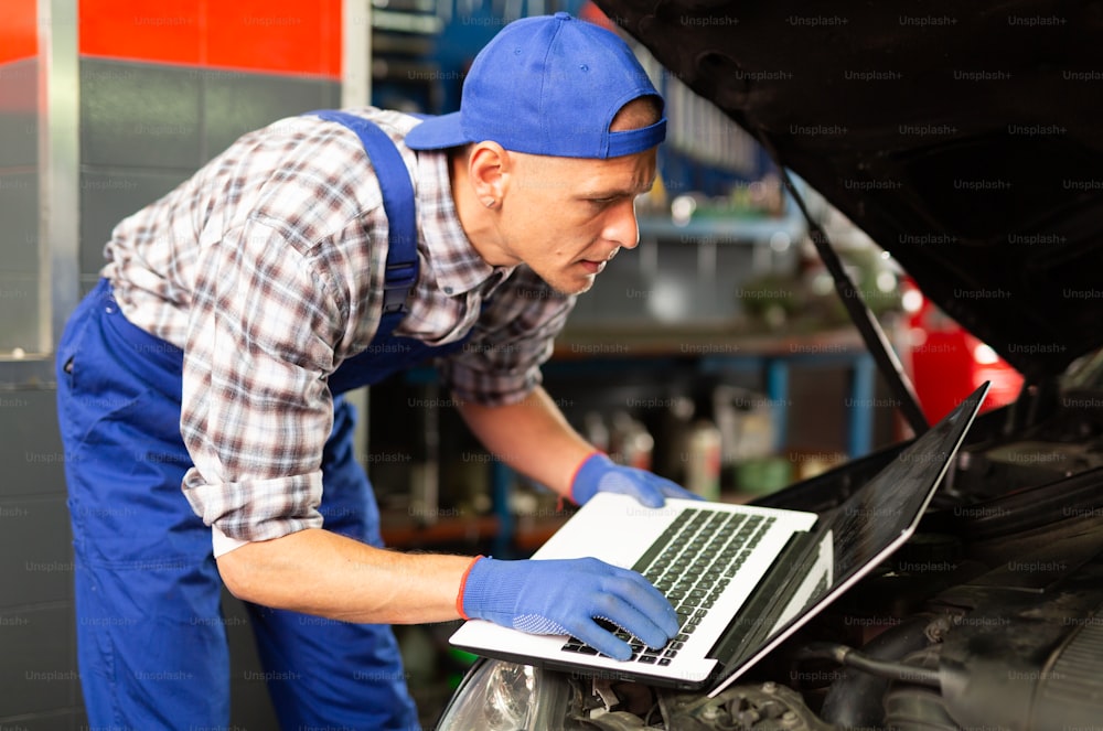 Mecánico con computadora portátil cerca del motor del automóvil en servicio automático