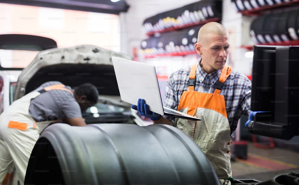 Mecánico con computadora portátil cerca del motor del automóvil en servicio automático