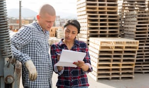 Confident woman manager discussing order list with man worker at warehouse of building materials