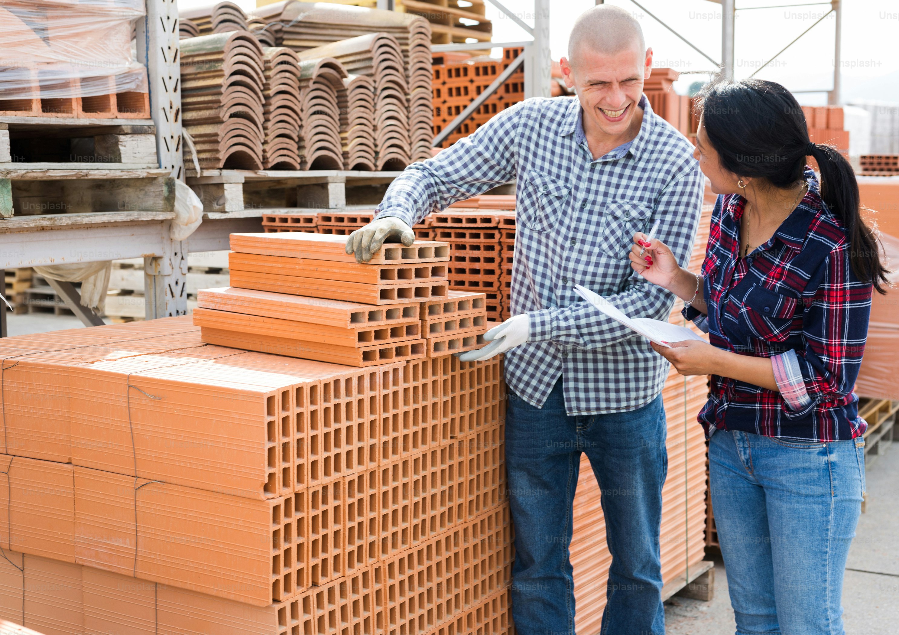 Colleagues man and woman collecting order of red bricks at warehouse of building materials