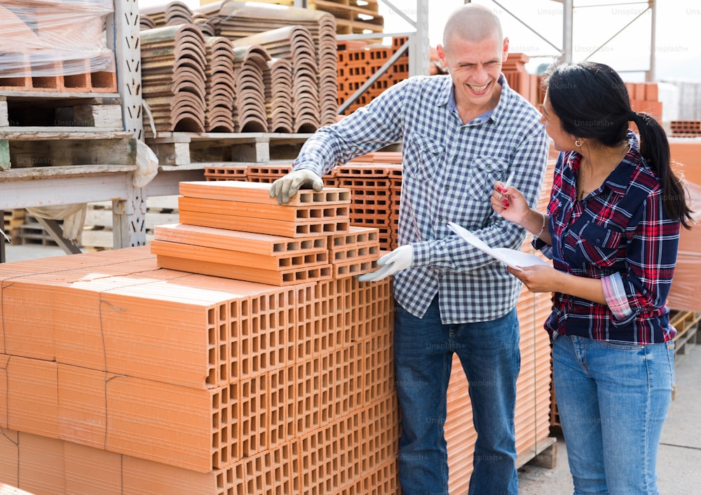 Colleagues man and woman collecting order of red bricks at warehouse of building materials