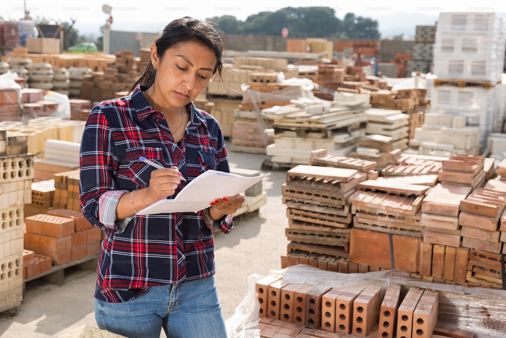 Concentrated hispanic woman worker controlling quantity of bricks at hardware store warehouse