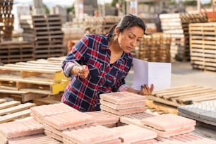 Concentrated hispanic woman worker controlling quantity of tiles at hardware store warehouse