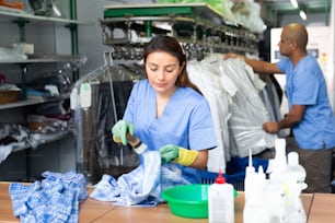 Ritratto della donna che pulisce la camicia dell'operaia della lavanderia usando la spazzola al negozio di lavaggio a secco