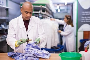 Tintorería hombre enfocado eliminando manchas y manchas limpiando camisa con cepillo