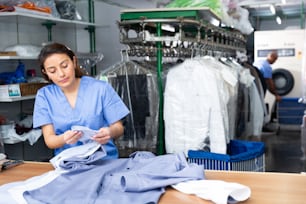 ドライクリーニング店で清潔なシャツをチェックする女性洗濯労働者のポートレート