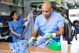Hombre seguro de sí mismo trabajador de lavandería limpiando camisa usando cepillo en instalaciones de limpieza en seco