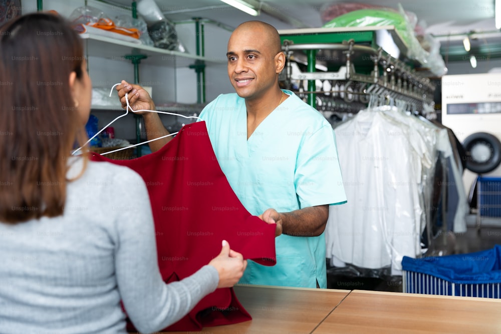 Homme souriant nettoyeur à sec donnant des vêtements propres au client, satisfait de la qualité