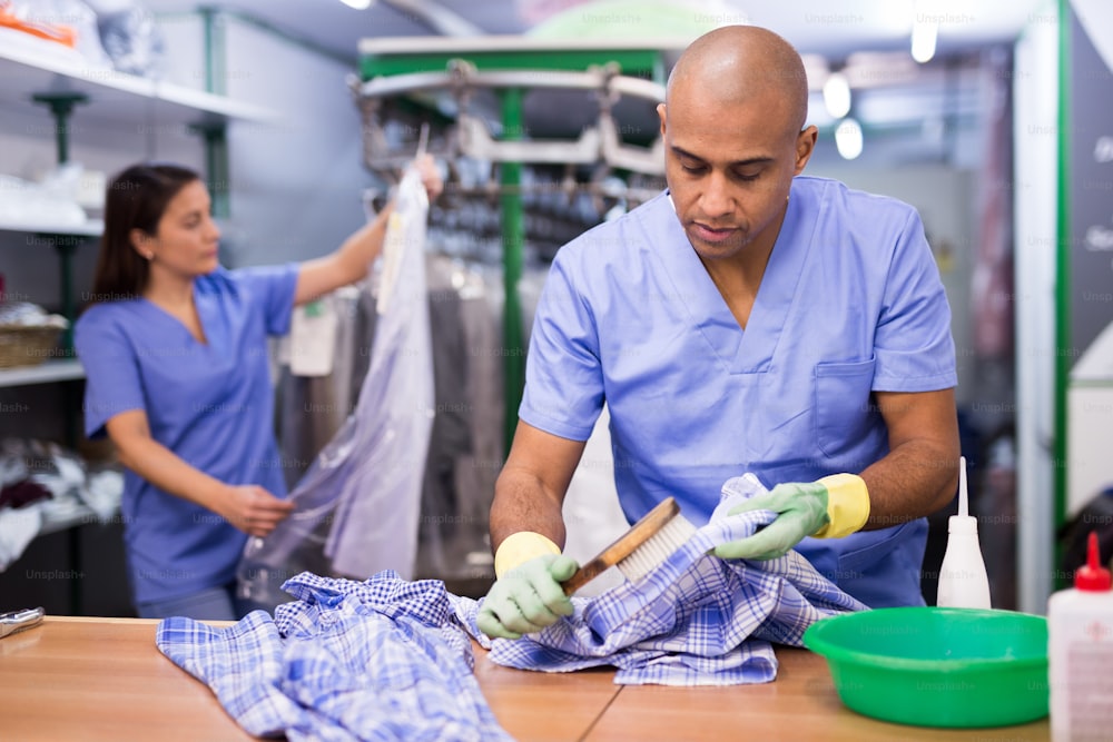 Confident man laundry worker cleaning shirt using brush at dry-cleaning facility