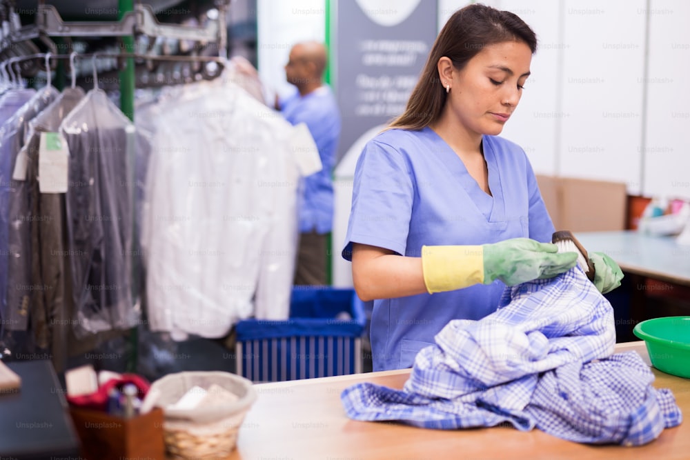 Tintorería hembra enfocada en eliminar manchas y manchas limpiando la camisa con productos químicos y cepillo