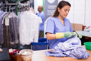 Focused female drycleaner removing spots and stains cleaning shirt using chemicals and brush