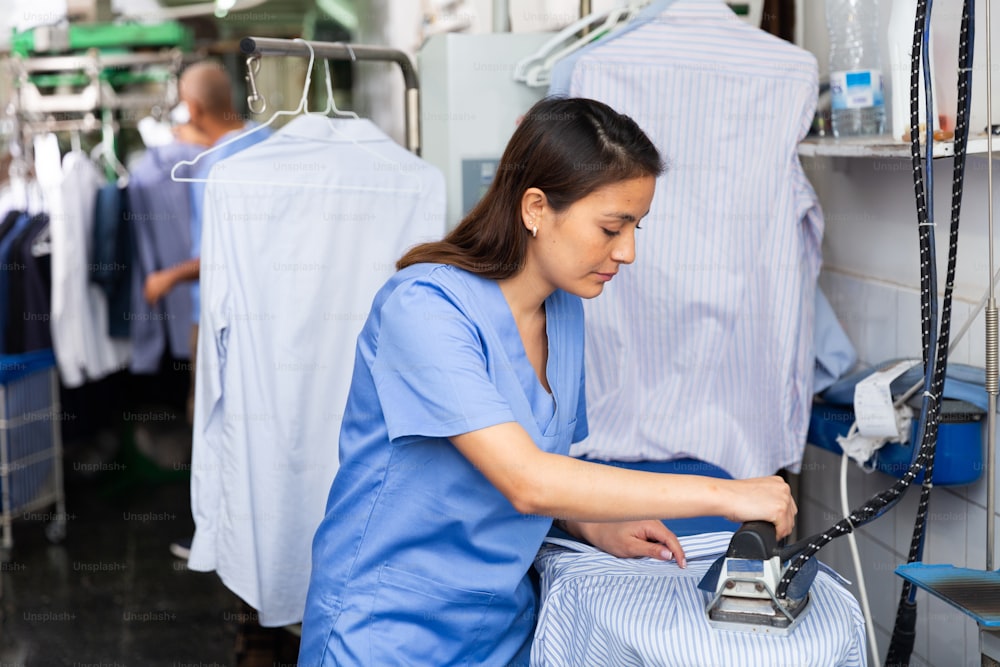 Trabajadora de lavandería enfocada planchando camisa en tienda de tintorería