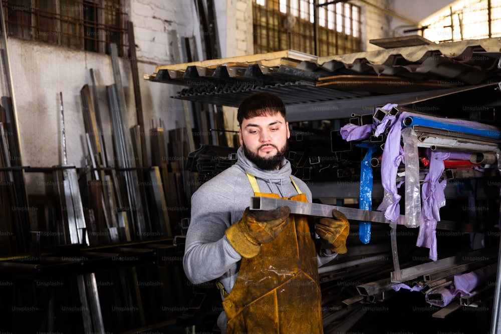 Cerrajero experto que trabaja en el taller mecánico de metalurgia, preparando tubos con forma para cortar