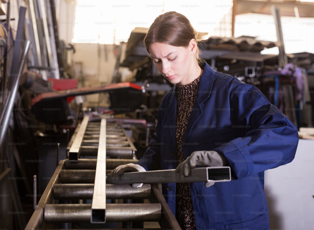 Trabajadora enfocada calificada que inspecciona la forma de las existencias de acero en el taller de corte de metales