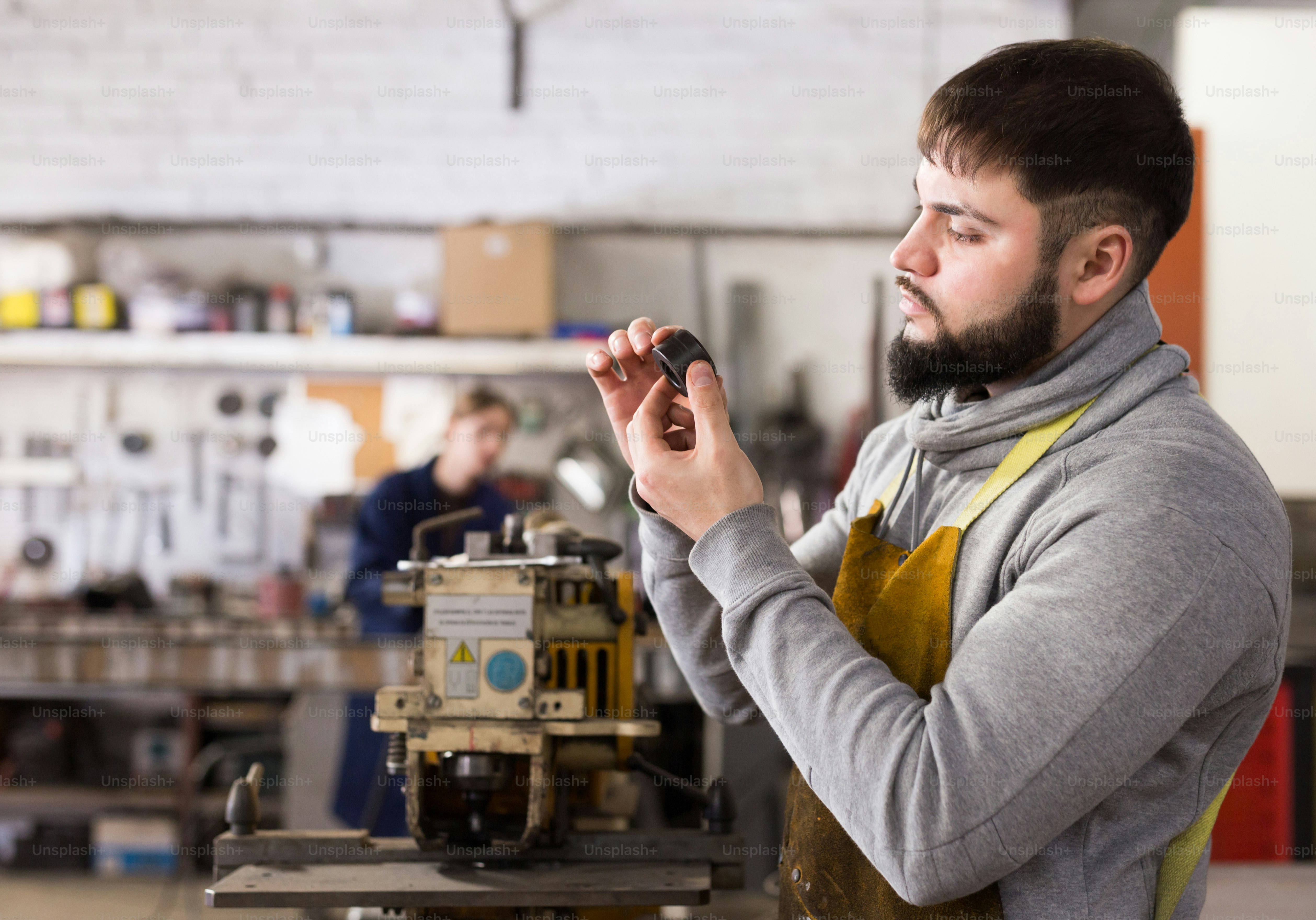 Porträt eines professionellen Arbeiters während der Arbeit in der Werkstatt, Frau im Hintergrund