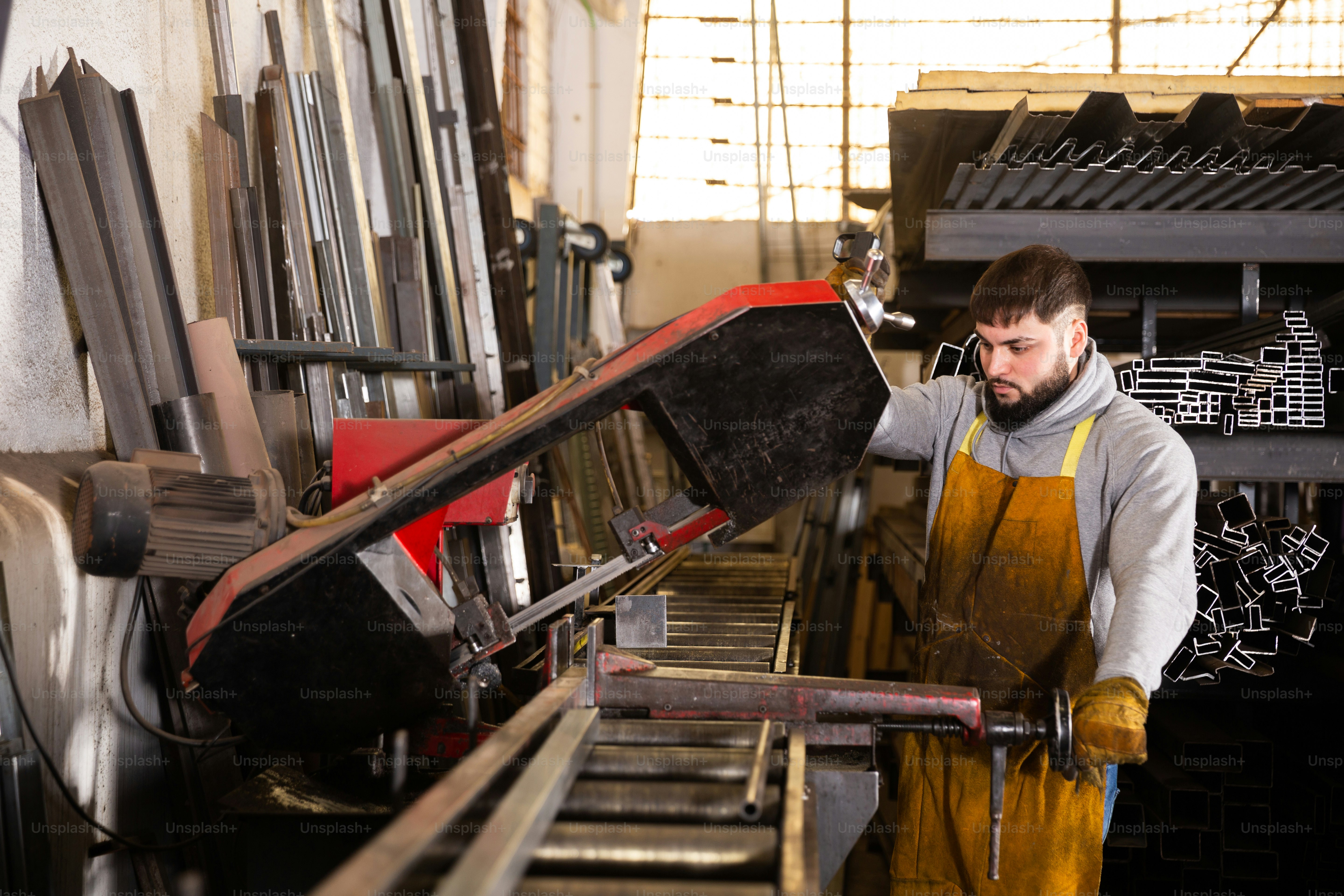 Focused bearded metalworker cutting square tubes on industrial band saw ...