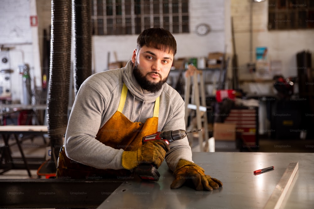 Retrato del hombre seguro de sí mismo taladrando chapa metálica en taller