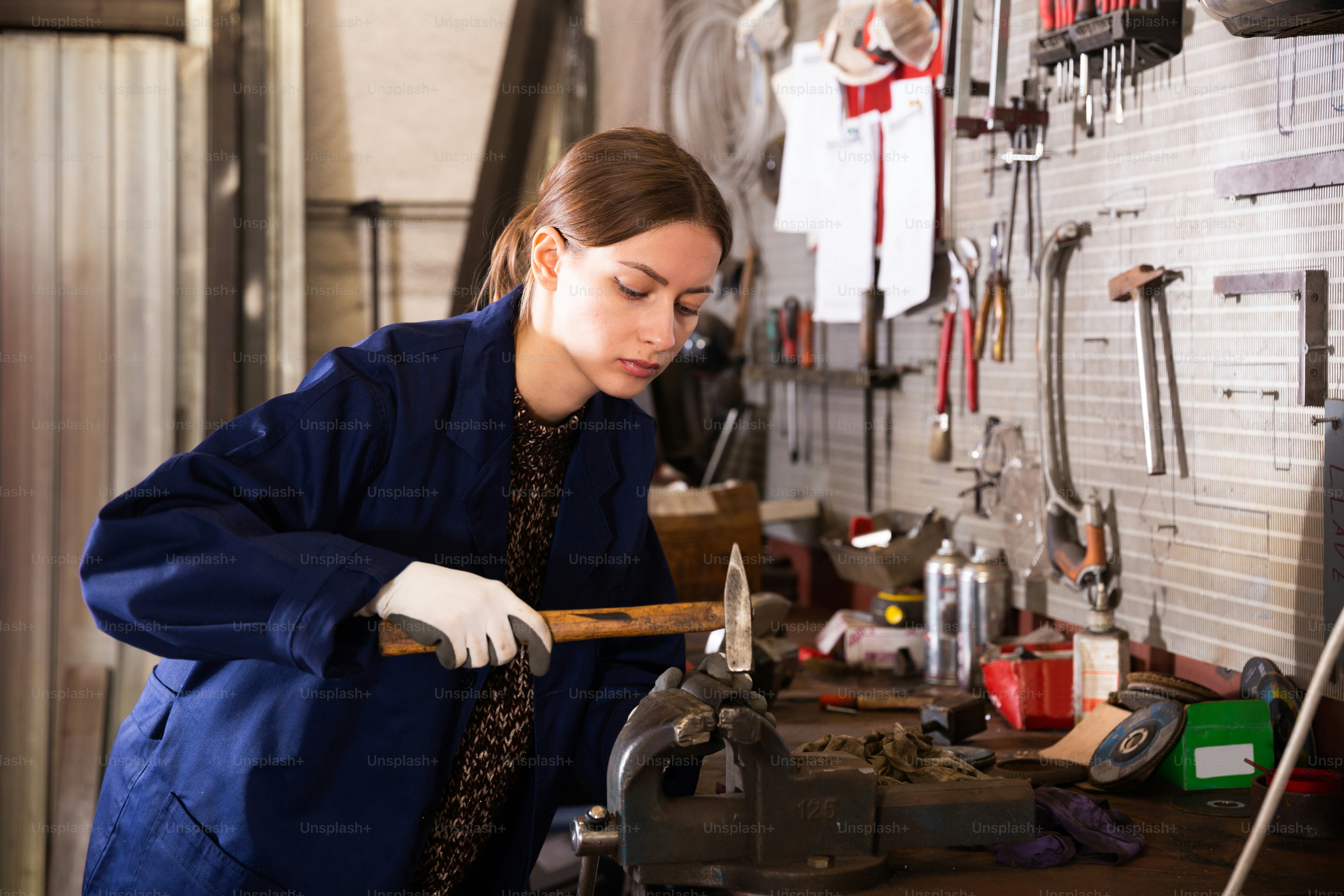 Junge Mechanikerin bei der Arbeit mit Handhammer in der Werkstatt