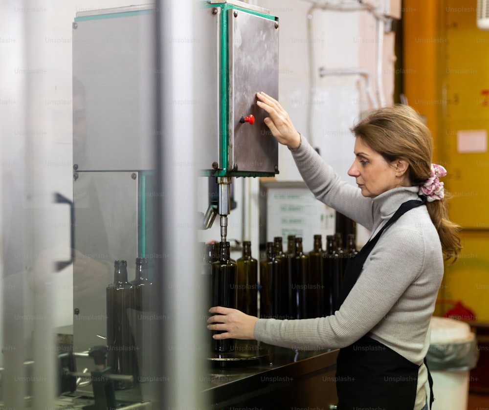 Experienced woman working on bottling line of artisanal olive producing oil factory