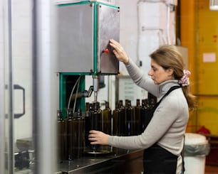 Skilled woman engaged in olive oil production, controlling process of bottling of finished product in glass bottles