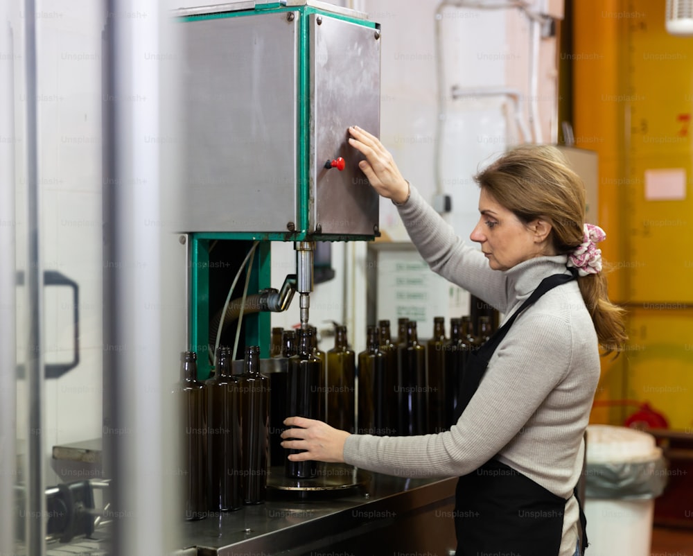 Skilled woman engaged in olive oil production, controlling process of bottling of finished product in glass bottles