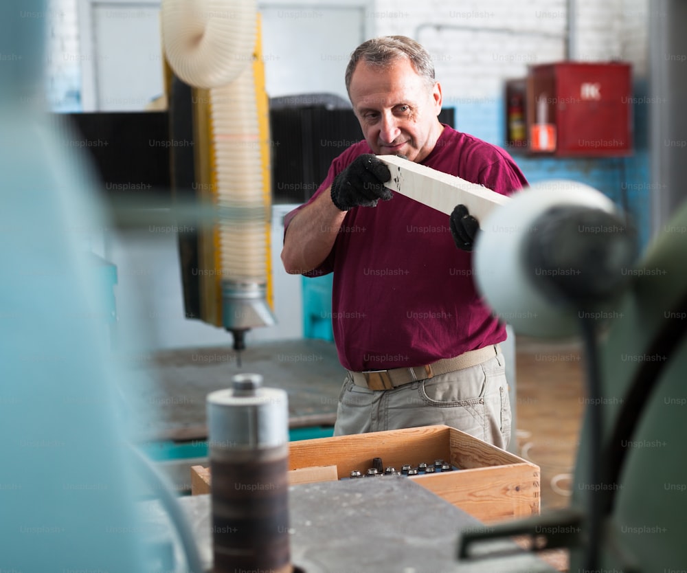 Concentrated worker is shaping timber on woodworking machine at the factory