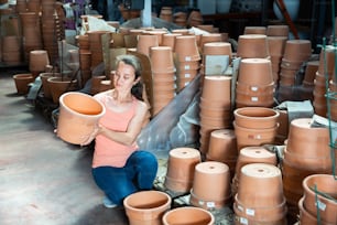 Female seller is standing near clay pots in stock