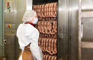 Frau überprüft die Qualität von gekochten geräucherten Würsten in einer professionellen Backmaschine in der Lebensmittelproduktionsfabrik