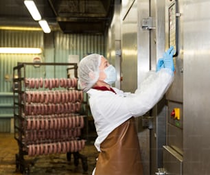 Trabalhadora que opera forno industrial de fumo para salsichas em fábrica de carne