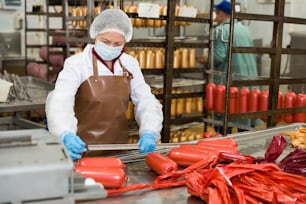 Fokussierte Frau hängt Rohwürste auf Schienen für die spätere Heißverarbeitung in der Fleischfabrik auf