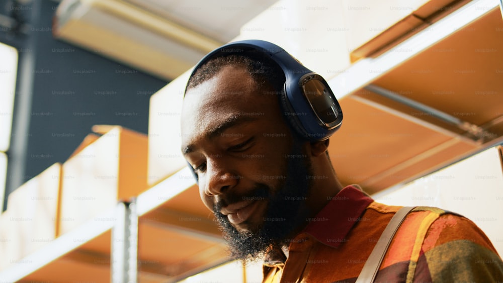 Male employee listening to music and working in depot, having fun dancing and using tablet to plan inventory. Young adult singing with headphones, working on stock production shipment. Handheld shot.