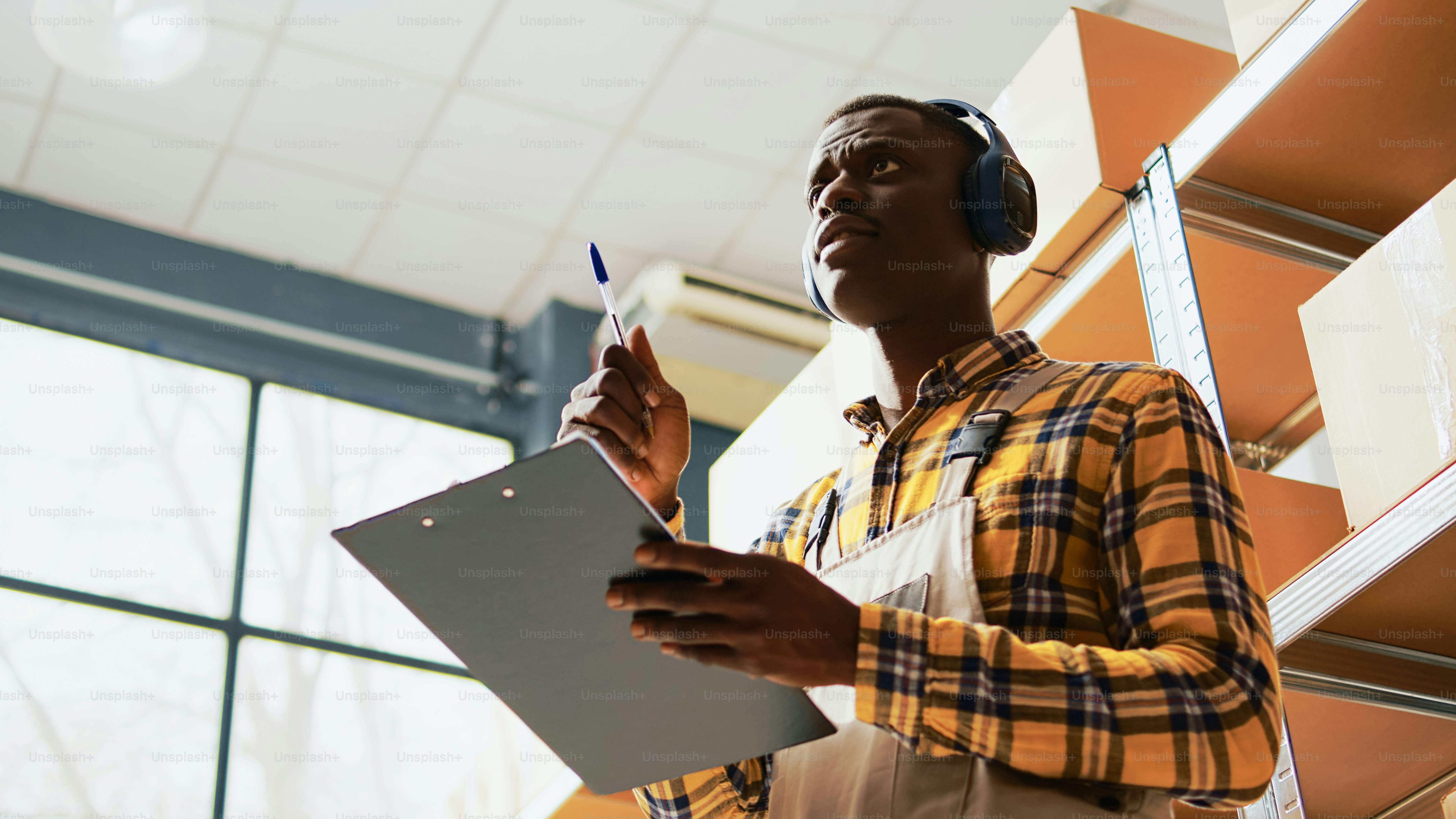 Young man singing and dancing in storage room, having fun listening to music on headset. Male depot worker showing dance moves enjoying merchandise or retail products. Handheld shot.
