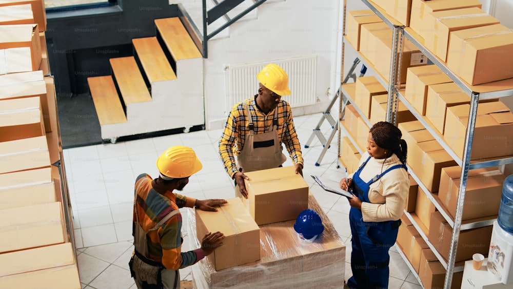 アフリカ系アメリカ人の人々は、商品を出荷するための品質管理を行う前に、製品を箱に詰めます。在庫と在庫ロジスティクス、小売出荷をチェックする倉庫従業員。ハンドヘルドショット。