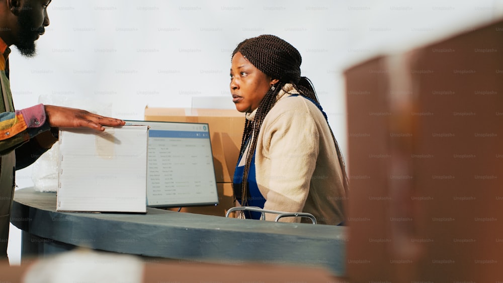 Depot worker planning stock logistics on computer, working with products in cardboard packages at warehouse. Woman working in storage room with goods and packages merchandise.