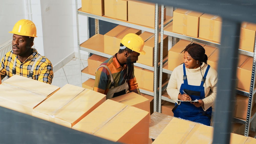Pessoas afro-americanas trabalhando em logística de estoque em armazém, verificando caixas de mercadorias na sala de armazenamento. Jovem equipe de funcionários do depósito fazendo inventário com lista de produtos.