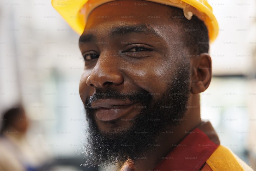 笑顔のアフリカ系アメリカ人の倉庫パッケージハンドラーの顔のポートレート。保管室で作業し、カメラを見る安全ヘルメットをかぶった運送会社の倉庫の従業員
