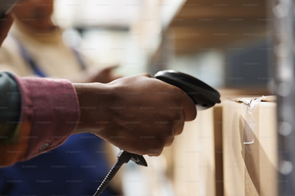 African american storehouse employee arm using barcode scanner on cardboard box. Warehouse operator hand checking merchandise carton bar code, holding digital scanning equipment close up