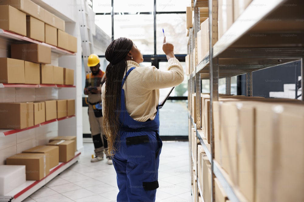 African american storehouse manager checking parcels maintenance and planning stock supply chain logistics. Warehouse supervisor standing near cardboard boxes shelf and looking upwards