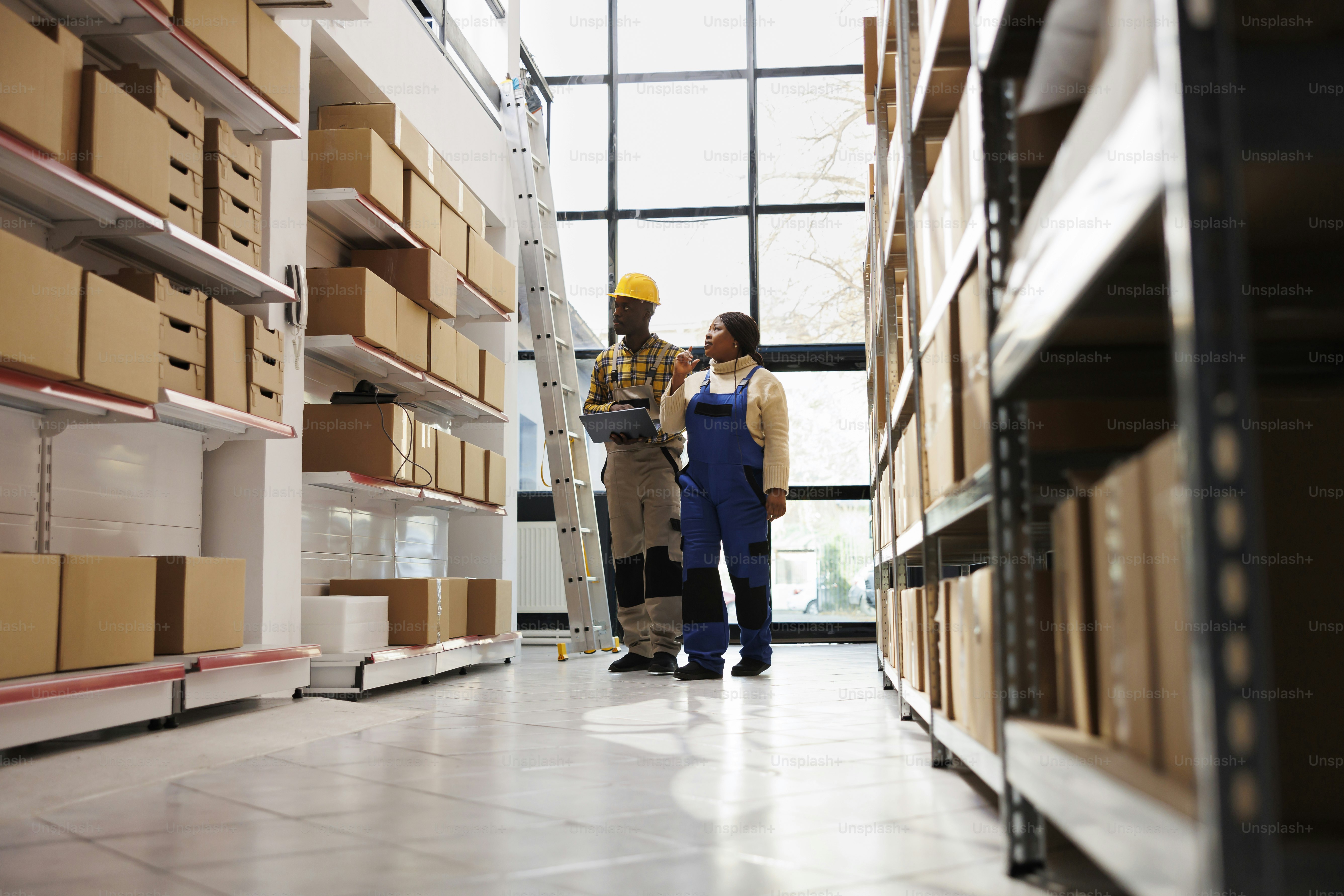 African american warehouse distribution manager doing inventory with assistant using laptop application software. Retail storehouse department operators supervising stock supply and maintenance