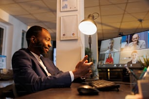 オンラインビデオ通話会議中にリモートの同僚に投資グラフを説明するアフリカ系アメリカ人のマネージャー。会社の統計オフィスのマーケティング戦略で深夜働くビジネスチーム