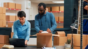 Diverse team of people working on supply chain packaging to prepare warehouse order. Two business partners packing merchandise and storehouse products after doing quality control.