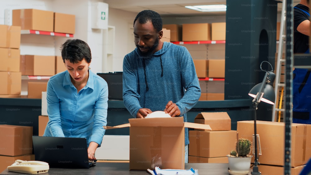 Diverse team of people working on supply chain packaging to prepare warehouse order. Two business partners packing merchandise and storehouse products after doing quality control.