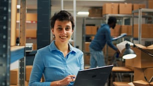 Trabalhadora verificando pacotes de papelão de prateleiras de sala de armazenamento, usando laptop para planejar o inventário de estoque e tomar notas. Empreendedor que atua no desenvolvimento de negócios e supply chain.