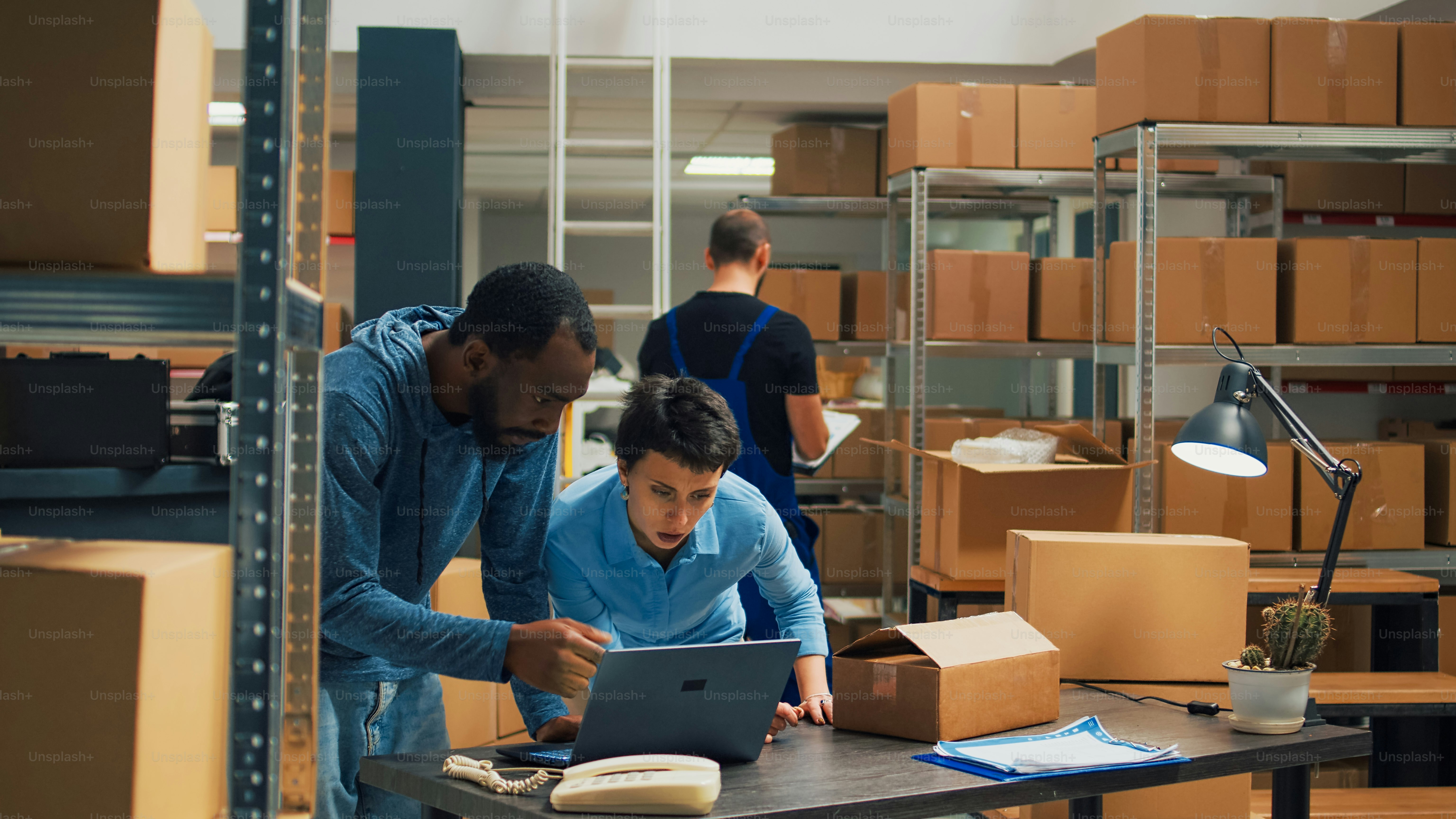 Büromitarbeiter, die Teamarbeit leisten, um Waren in Kartons zu versenden und die Qualität der Waren im Lager zu überprüfen. Verschiedene Besitzer, die einen Laptop verwenden, um die Verteilung des Produktversands zu planen.