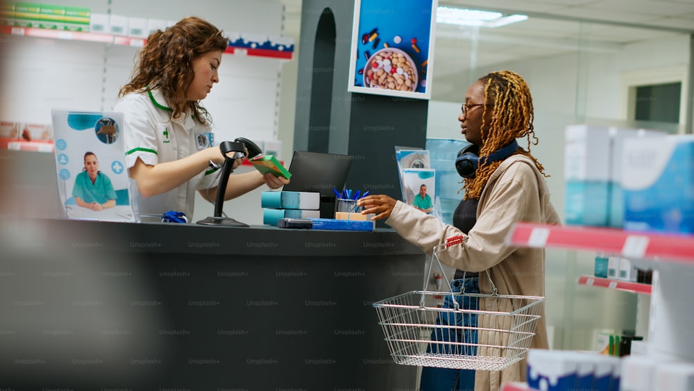 Pharmacist selling medical products to african american client, buying medicaments and supplements at pharmacy desk. Worker scanning boxes of drugs and vitamins to sell medicine. Handheld shot.